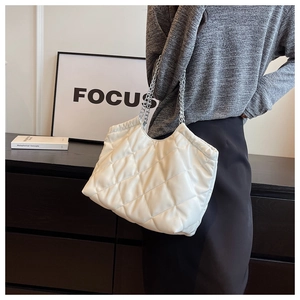 Close-up of white quilted tote bag with silver chain strap shown in a modern lifestyle setting