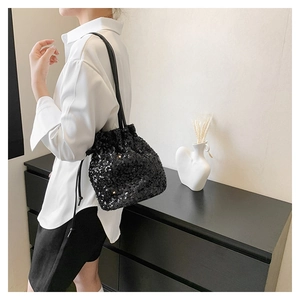 Détail du sac seau à paillettes noires avec cordon de serrage sur un mannequin élégant