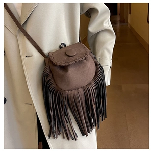 Detail of a brown suede saddle bag with handmade woven edges and long tassel fringe