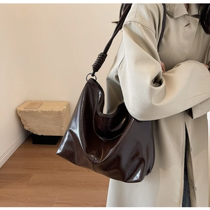 Detail of a large dark brown tote bag with glossy finish and spiral knot strap design
