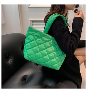 Detailed view of a green quilted tote bag worn by a model in a black sweater