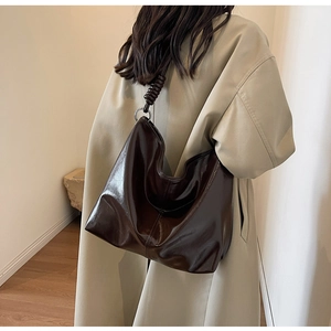 Detail of dark brown glossy hobo bag with a twisted shoulder strap and silver ring hardware
