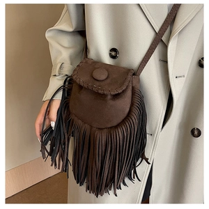 Brown suede crossbody saddle bag with long fringe tassels shown on a beige trench coat