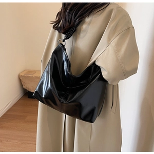 Detail of glossy black hobo bag featuring woven rope strap and metallic ring connectors