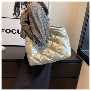 Detailed close-up of a silver quilted tote bag with metallic texture and chunky chain strap