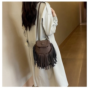 Brown faux suede saddle bag with fringe detail worn over a beige coat for a stylish autumn look