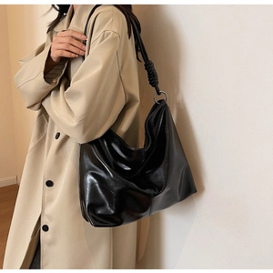 Detail of black glossy leather hobo bag with braided knot and silver ring accents on model