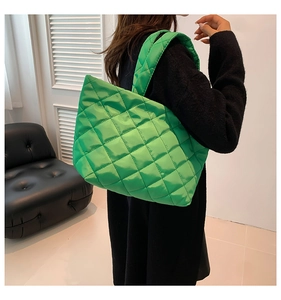 Green quilted down tote bag with a glossy finish and spacious puffy design worn by a model