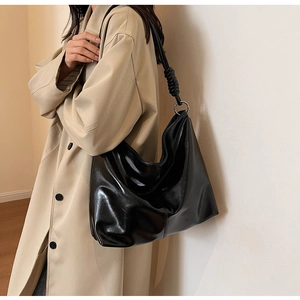 Model wearing a large black shiny leather shoulder bag with thick knot strap and silver ring