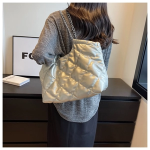 Silver quilted tote bag with chain strap shown on model in a minimalist setting