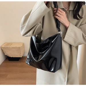 Detail of glossy black leather tote bag featuring unique spiral twisted shoulder straps