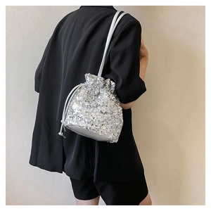 Sac seau à paillettes argentées avec cordon, porté sur un costume noir chic de soirée