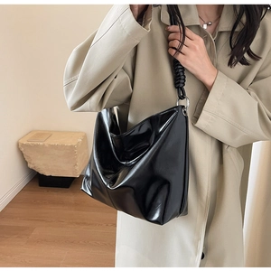 Close-up of a glossy black tote bag with braided rope strap detail and metallic rings