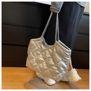 Silver quilted tote bag with metallic sheen and chain straps in a modern indoor setting