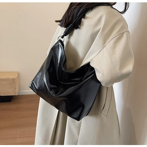 Detail of black glossy faux leather hobo bag with unique spiral shoulder strap design