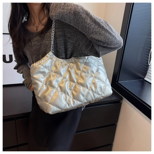 Detail view of silver quilted tote bag with metallic chain strap worn by a model