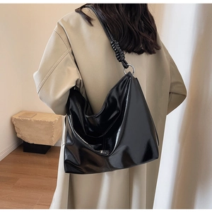 Detailed view of glossy black hobo bag featuring twisted strap knots and silver metal rings