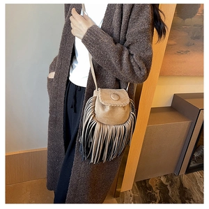 Detail of suede crossbody bag featuring long tassels and hand-woven stitching accents