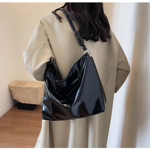Detail of high-gloss black hobo bag with unique spiral shoulder strap on model