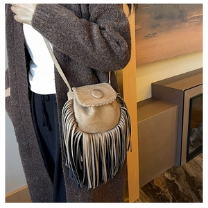 Detail of khaki faux suede crossbody saddle bag featuring long fringe tassels and flap closure