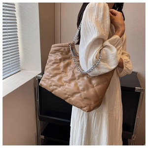 Detail of quilted khaki tote bag with silver chain strap shown on model's shoulder