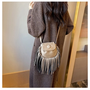 Detail of bohemian khaki suede tassel saddle bag worn by a model in warm indoor setting