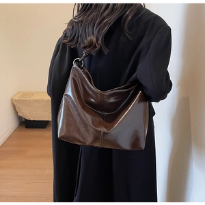 Detail of dark brown glossy patent leather hobo bag with silver ring hardware and stitching