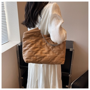 Rear view of model wearing a caramel quilted tote bag with silver chain straps