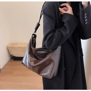 Detail view of glossy dark brown leather shoulder bag with twisted knot strap design