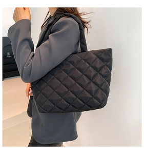 Side view of model wearing a large black quilted tote bag with padded shoulder straps