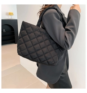 Side view of large black quilted tote bag with wide padded shoulder strap worn by model
