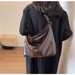 Detailed close-up of dark brown glossy leather tote bag with thick rope knot shoulder strap