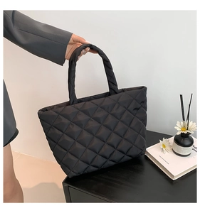 Detail view of large black quilted tote bag with soft padded handles and glossy finish