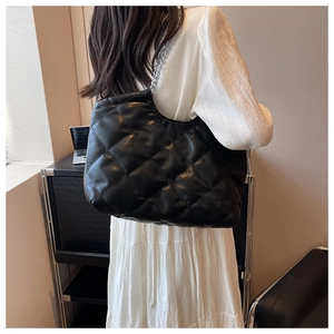 Close-up of black quilted tote bag featuring silver chain strap on a white dress model