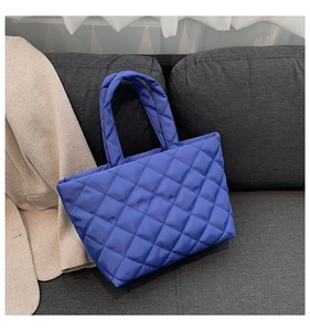 Detailed view of royal blue quilted tote bag on grey sofa with beige blazer accessory