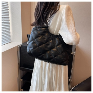Detail view of black quilted tote bag with silver chain strap on a model's shoulder