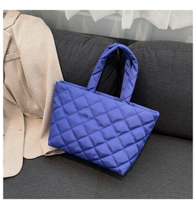 Detail of royal blue quilted tote bag in shiny nylon fabric on a grey fabric sofa