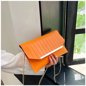 Detail der leuchtend orangen Umschlagtasche mit vertikalen Falten und goldener Kette