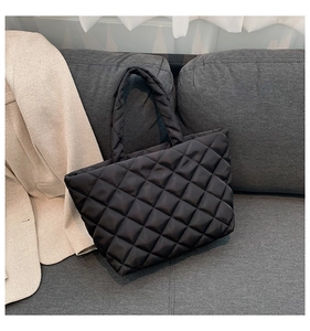 Detail of black quilted tote bag featuring classic diamond stitching on glossy nylon fabric