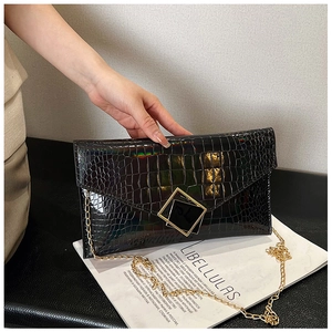 Close-up of black stone texture envelope clutch with gold metal buckle and chain strap