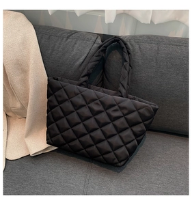 Close-up of black quilted puffer tote bag on a grey sofa showing texture and soft material
