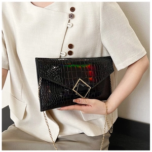 Detail of black crocodile texture envelope bag with iridescent finish and gold metal buckle