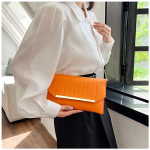 Detail einer orangefarbenen Umschlagtasche mit Goldleiste und feinem Kettenriemen