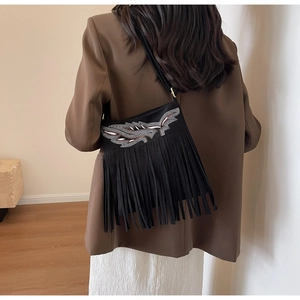 Détail du sac seau noir en daim avec broderie d'ailes, strass et longues franges