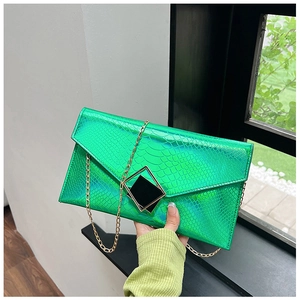 Pochette verde con stampa serpente e catena dorata tenuta davanti a piante esterne