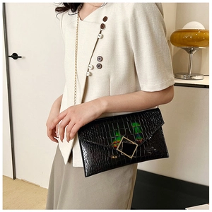 Detail of black crocodile texture envelope bag with gold square buckle and chain strap