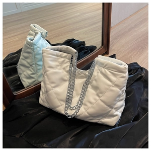 Detailed macro view of white quilted tote bag featuring silver chain straps and stitch texture