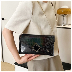 Detail of black crocodile pattern envelope bag with gold chain strap on model
