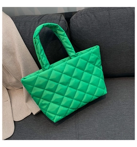 Detail view of the green quilted puffer tote bag on a grey sofa for autumn style