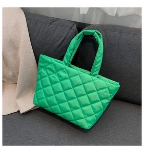 Detailed close-up of light green quilted tote bag with diamond pattern on a gray sofa